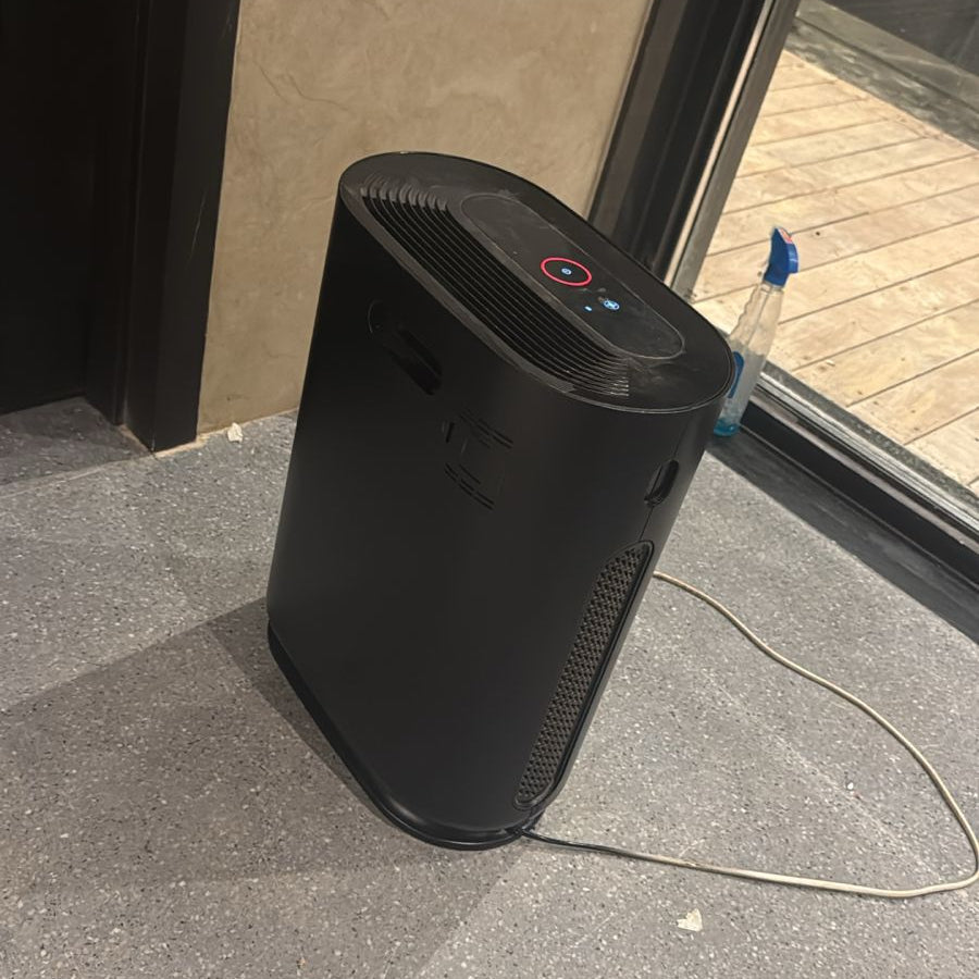 Black air purifier on a gray floor next to a glass door.