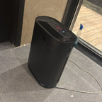 Black air purifier on a gray floor next to a glass door.